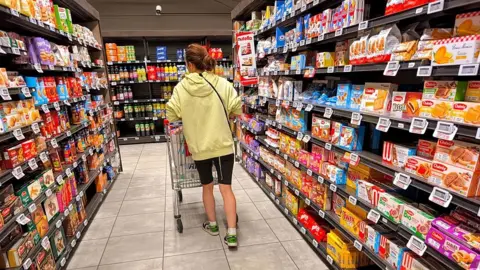 AFP via Getty Images A woman shops pushes her shopping cart through a cake and biscuit aisle at an Intermarché supermarket in France.