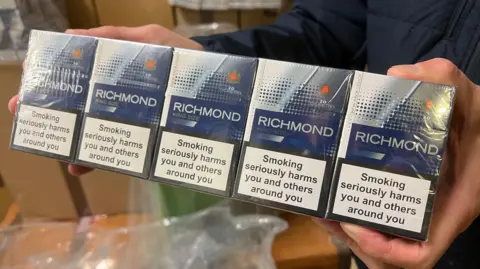 Two hands hold up five blue Richmond cigarette boxes inside a lock-up