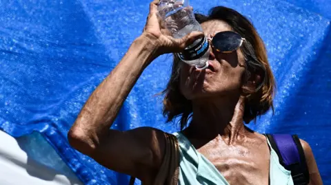 A woman drinks water while cooling down in a tent in Phoenix's largest homeless encampment, amid the city's worst heat wave on record on 25 July , 2023