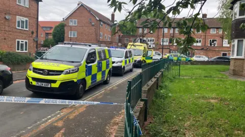 Police vans and ambulances in a cordoned off residential street.