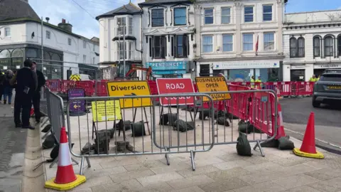 Road signs and barriers surround holes in the road at the bottom of Market Jew St in Penzance