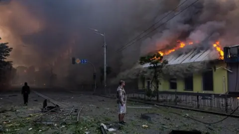Reuters A man looks at a burning building set ablaze during an overnight Russian missile and drone strike
