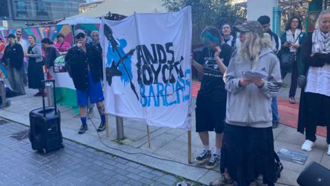 A protest and a banner which reads "bands boycott Barclays"