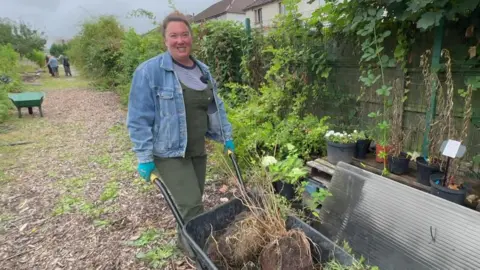 Victoria Holden is pushing a wheel barrow of dead plants along the path at the community garden.