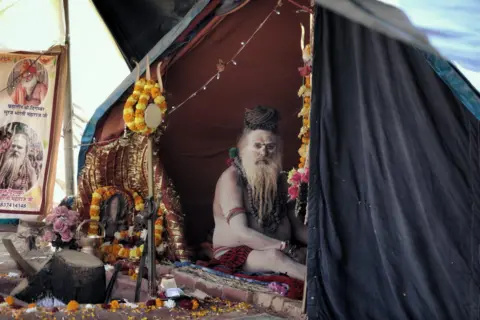 an ash-smeared ​Hindu holy man sits in a tent‌ at the Kumbh‍ Mela festival in Prayagraj in⁣ January 2025