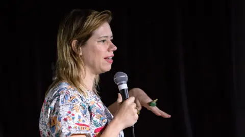 Getty Images Lou Sanders wearing a colourful top and holding a microphone