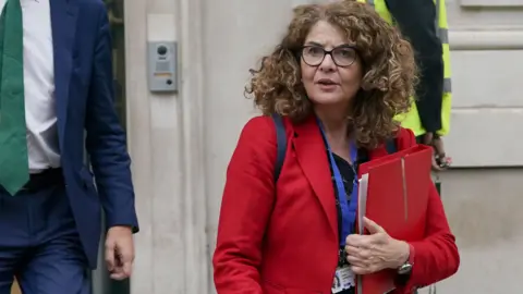 PA Media Policing minister Diana Johnson leaves the Cabinet Office in Westminster, central London wearing a red coat.