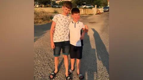 Supplied A holiday photo of Bobby and Shay when they were younger. They are wearing dark shorts and white t-shirts and sliders, and both smiling at the camera.