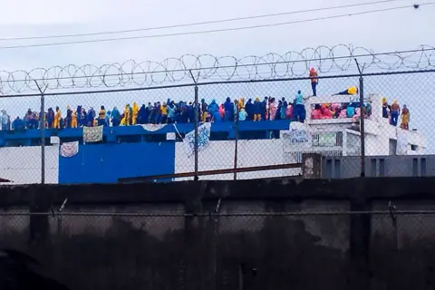 Inmates dressed in prison jumpsuits can be seen during a protest at the prison in Barinas state. They have hung sheets bearing messages from the roof.