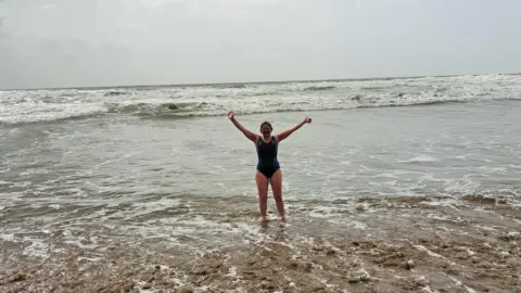 Helen Jewell Helen Jewell in her swimming costume, standing in the shallows of the sea with waves behind her