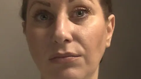 A police mugshot of Alexandra Power, 40, who has light brown hair tied back and wears a pink and white striped t-shirt. 