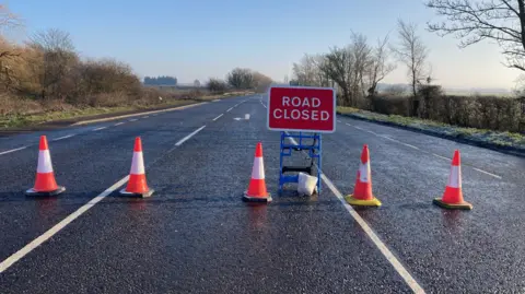 A row of traffic cones and a sign reading Road Closed placed across a road