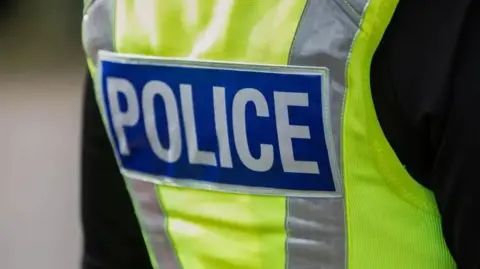 The back of a high-vis police vest with the word POLICE on the back written in white letters on a blue background