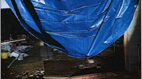 A hole in the ceiling with blue tarpaulin falling down.