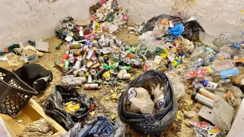 Gill Thomas The photo shows black bags of rubbish. There is a large pile of cans, bottles and other household waste.