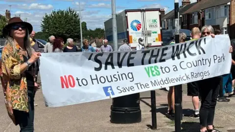 Richard Smith/BBC Campaigners holding up a banner which reads Save The Wick during a protest in the road. The banner reads 'Save the Wick'.