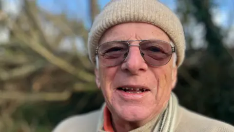 A man with a cream coloured hat and top and glasses.