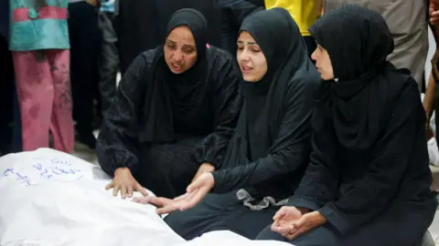 Reuters Women mourn beside body bags at the Indonesian hospital, northern Gaza (14 May 2025)