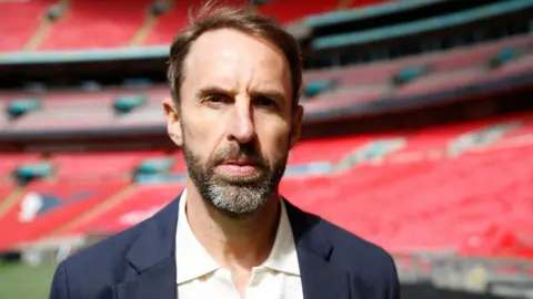 Gareth Southgate has a neutral expression in a picture posed in a football stadium.