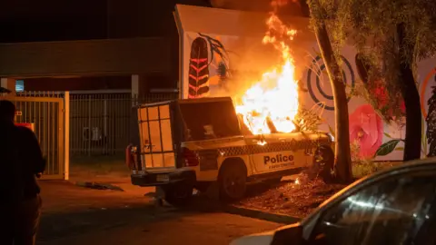 A police vehicle is set alight during clashes between community members and law enforcement outside Alice Springs Hospital.