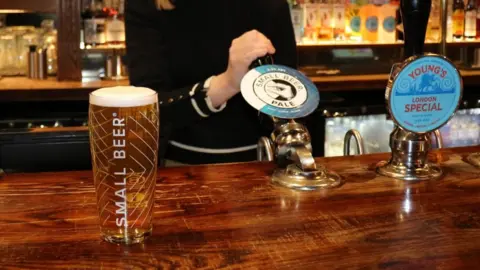 Small Beer Brewery A pint sits on the bar to the right of the table whilst a woman pours a pint of the Small Beer Pale.