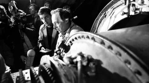 Getty Images Black-and-white photograph of Donald Campbell talking to reporters in November 1966. He has dark hair, brushed back from his face. 