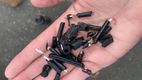 An outstretched palm containing lots of bits of partially chewed black wiring from Lauren Brook's car