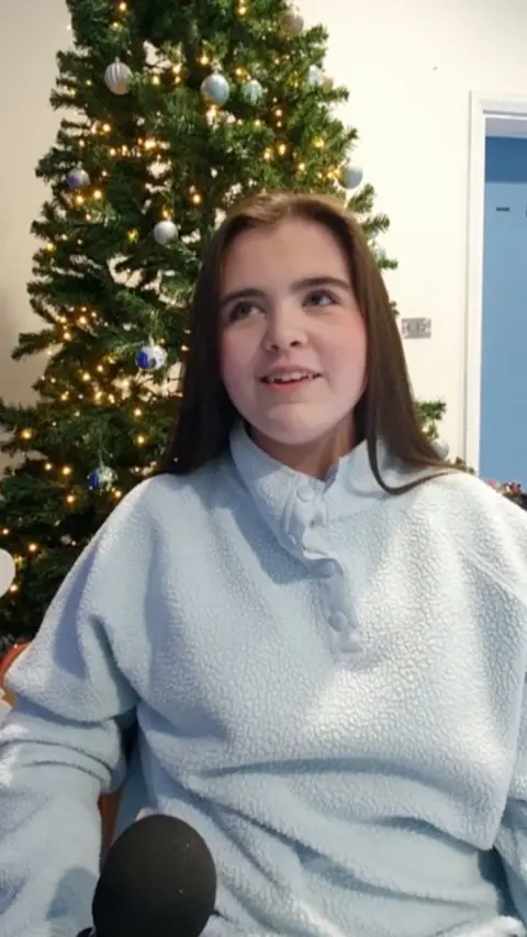 Maire is wearing a light blue fleecer and has long brown hair.