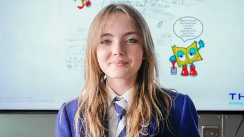 Story Shop A schoolgirl, wearing blue school uniform, in front a white board detailing her heated blanket idea