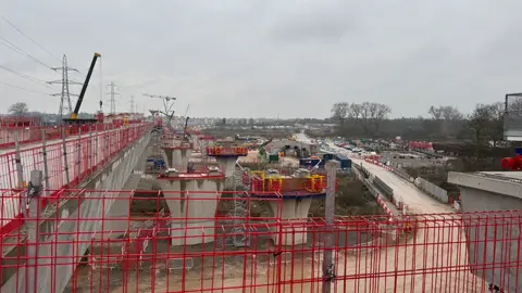 The River Tame West Viaduct being built - red fences cordon off the engineering works, with huge, half-finished concrete supports in the distance 