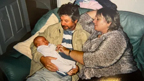 LaTonya as a newborn baby being held by her two grandparents lying on a couch