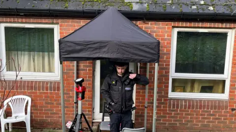A police officer stood outside a flat in Dorking. A gazebo is placed over the door to cover it.
