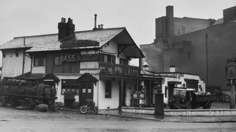 Getty Images Black and White Photo of You Olde Swiss Cottage Pub is rolling a barrel with a man in 1948