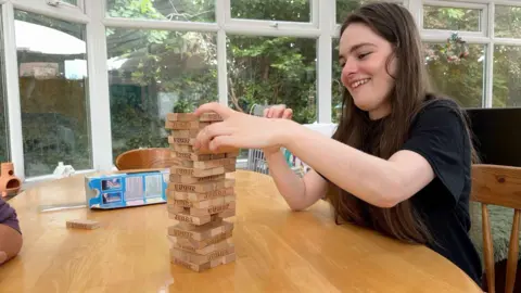 A woman sits at a table playing with wooden jenga blocks.