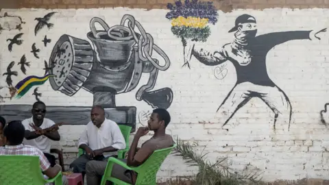 Getty Images People drinking tea or coffee in front of a mural drawn in the style of Banksy - Khartoum, Sudan