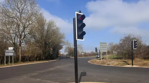 Wiltshire Council A traffic light on a road which has no road markings on it. It is a crossroads.