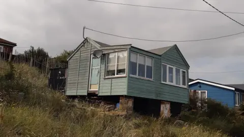 Andy Sloan Andy Sloan's green challet perched on a grassy dune. A blue chalet is in the background.