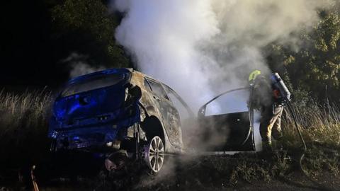 A fire fighter putting a car fire out in Matching Green, Essex