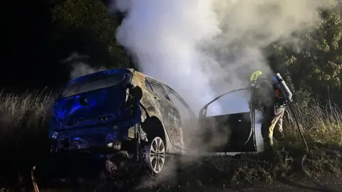 Stansted Fire Station A fire fighter putting a car fire out in Matching Green, Essex