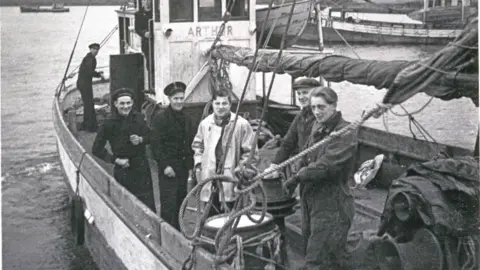 A black-and-white image of men on a fishing boat looking at the camera.