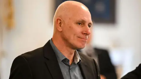 David Kelly wearing a grey shirt and black jacket