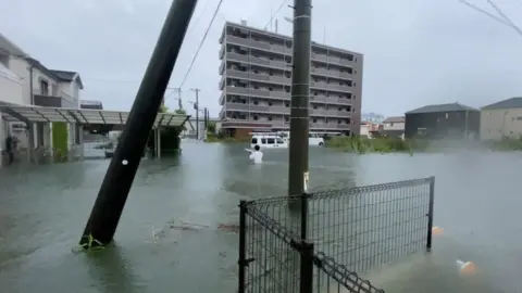 @Napspans via Reuters A person walks at a flooded area during heavy rain in Kurume, Fukuoka Prefecture