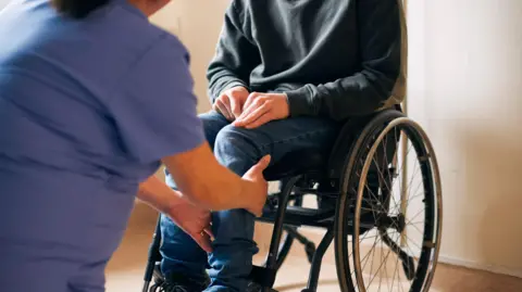 Getty Images Midsection of female healthcare expert examining leg of patient sitting on wheelchair in medical clinic