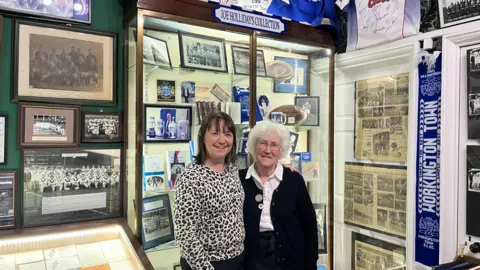 Tricia Poole and Dorothy Holliday, posing in front of the Joe Holliday collection at the Helena Thompson Museum.