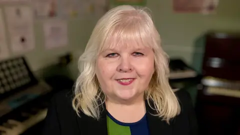 Martin Giles/BBC Head and shoulders image of Maria Grimmer, wearing a dark suit jacket and blue and green top