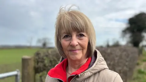 Kath Hardman who has blonde short hair wearing beige coat