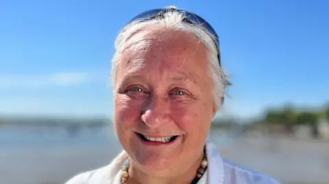 Martin Giles/BBC Ruth Leach smiles at the camera. She has grey hair that has been tied back behind her head. She wears sunglasses on top of her head as well as a white shirt.