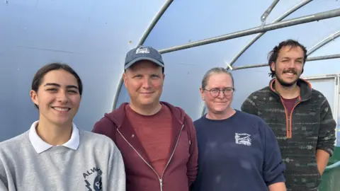 BBC/Louise Hobson Four members of the Tees Rivers Trust are stood in a polythene tunnel. Faith Andrews on the left is smiling and wearing a grey jumper. Marc Stokes is wearing a red hoodie. Judy Power is wearing a blue jumper and Adam Rounce is wearing a patterned green fleece.