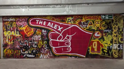 David Platt A wall of graffiti art, with a large red hand in the middle, with one finger pointing to the left, with the words The Alex in it