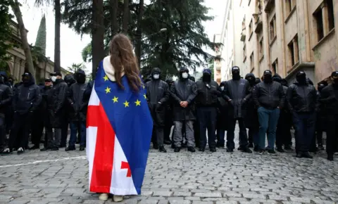 Reuters A protester wearing a Georgian and European flag faces off policemen blocking a street during a rally against a draft bill on 'foreign agents' near the Parliament building in Tbilisi, Georgia